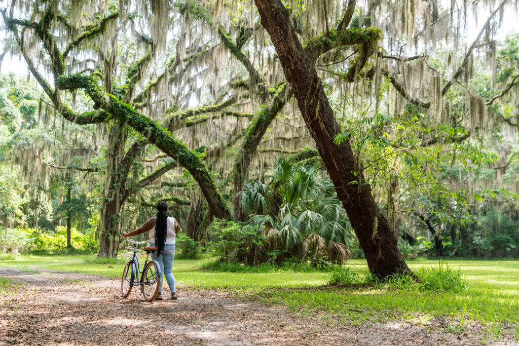 Woman with bike underneath live oak trees.